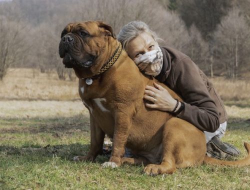 Woman wearing a mask cuddling with a dog